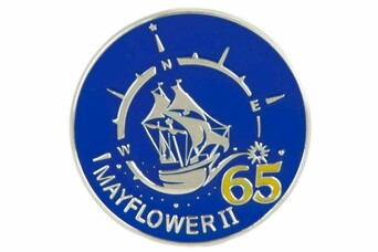 A blue pendant with a silver design depicting Mayflower II in a compass and 65 written in yellow