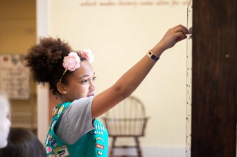 Girl scout raises arm to point at object behind glass in case