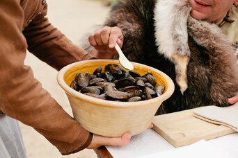 pilgrim serves mussels to seated guest