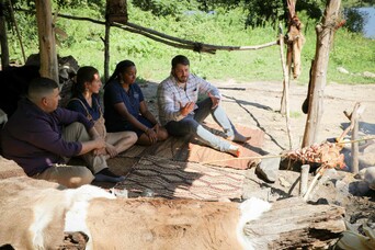 Two women and two men sit and talk in outdoor cooking arbor