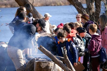 Museum educator demonstrates how to make a mishoon to a group of elementary school aged students