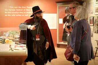 Pilgrim speaks with a man and woman in an exhibition space