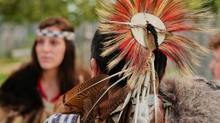 A seated man and woman wear regalia