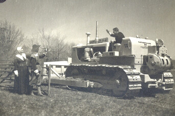 A man in a tank wearing a business suit waves to a man and woman dressed as Pilgrims