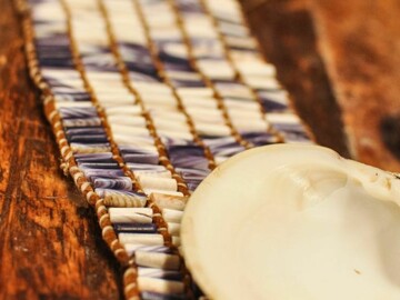 Belt made of purple and white wampum with quahog shell arraigned on top of the belt