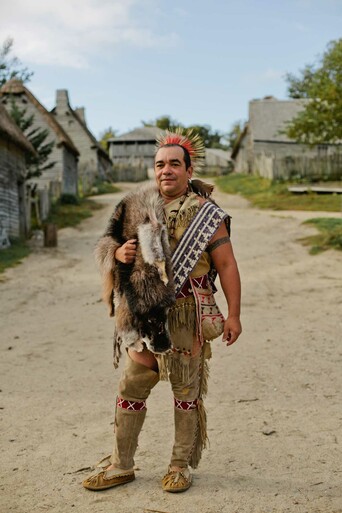 Man in Wampanoag regalia models wampum belt in 17th century English Village