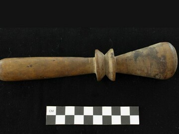 Turned pestle made of wood. Tapered handle with two inverted cones separating from conical hammer surface.