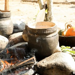 Wampanoag cooking pots set over an outdoor fire. A bowl with orange pumpkins is in the background.