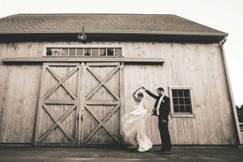 Groom spins his bride in front of a rustic barn