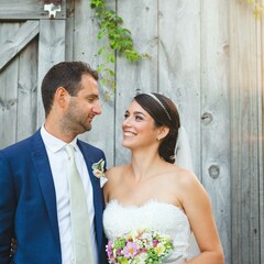 Bride and groom smile at each other in front of a barn