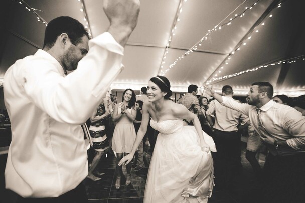 Bride and groom dance with wedding guests under a tent