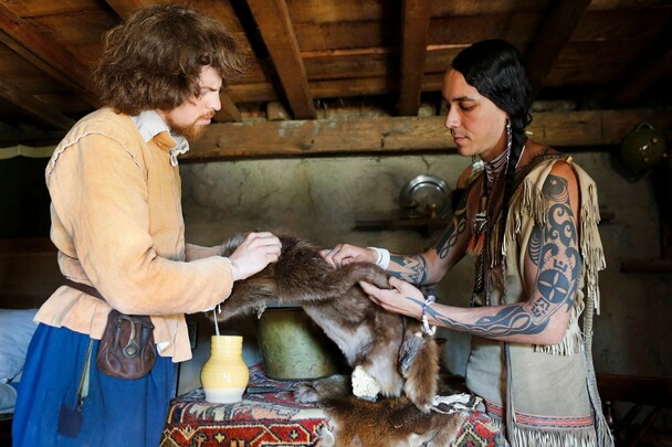 Wampanoag man and Pilgrim man inspect a fur pelt for trade.