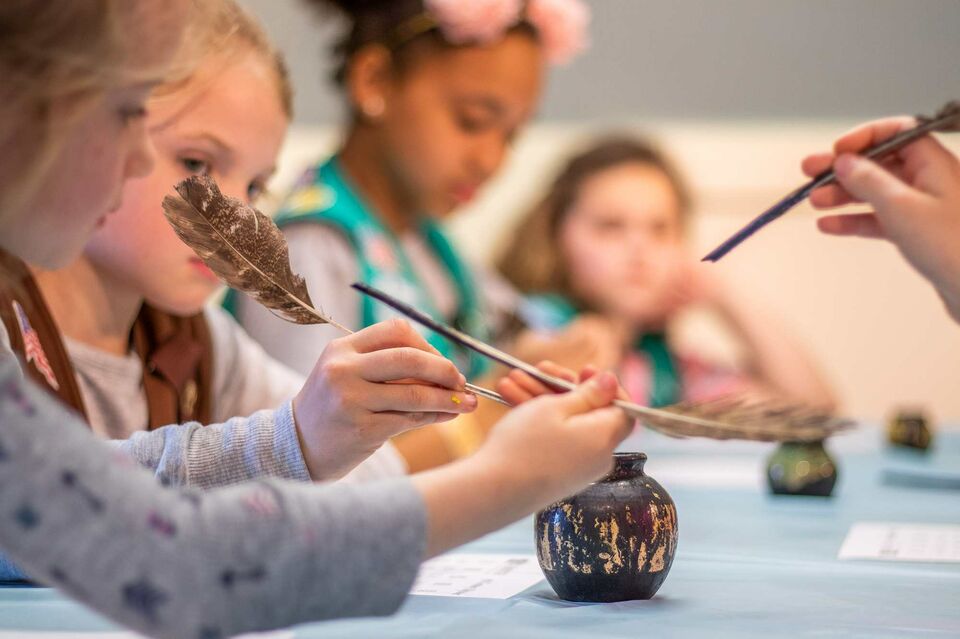Girl scouts dip quill pens into inkwell